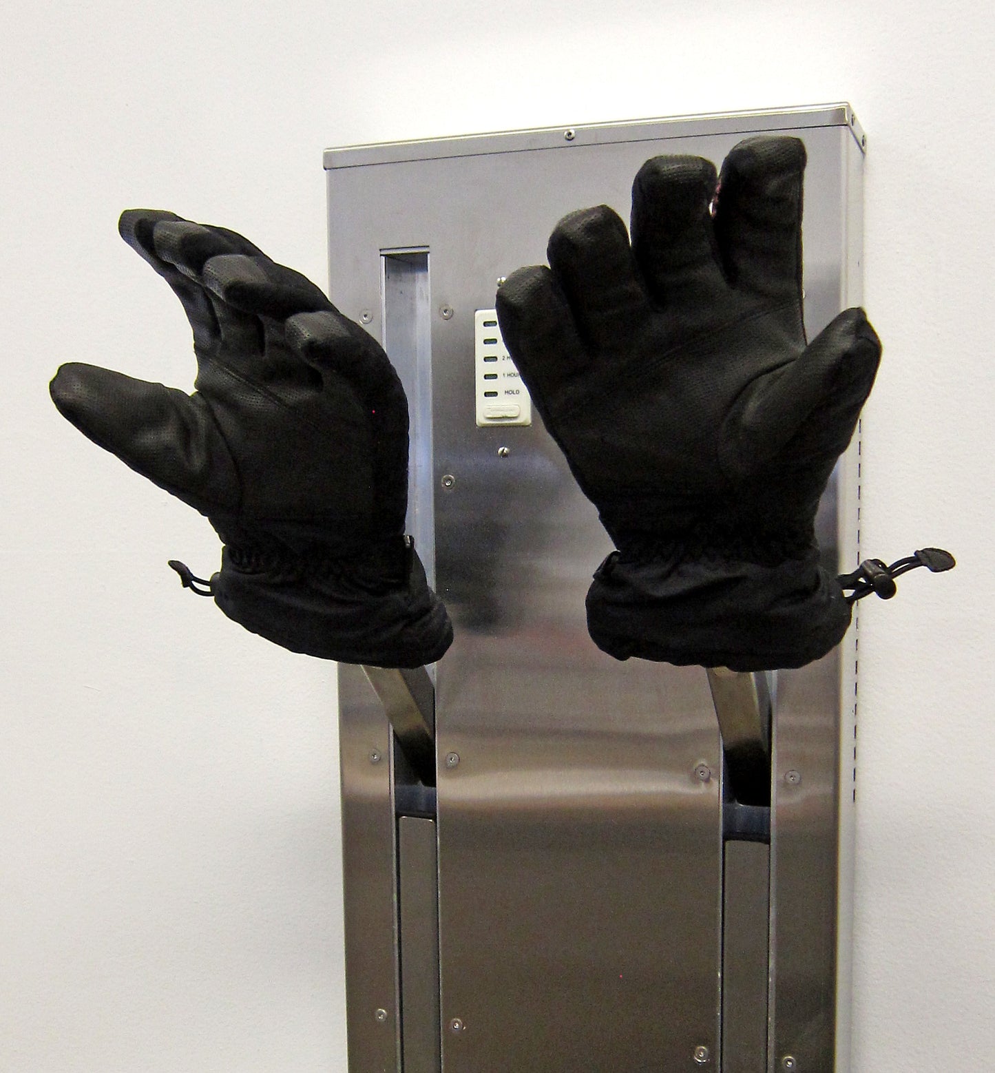 Glove dryer of stainless steel for fast drying of ski gloves. Installed on a boot dryer with retracting pegs for installation in mudroom or ski condo. Shown with gloves held for fast drying with warm air forced up fingers. 